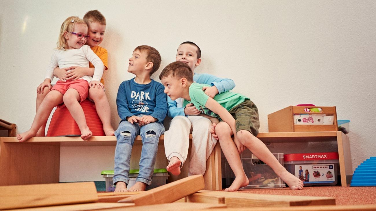 Mehrere Kinder sitzen zusammen in einer Spielecke mit Spielzeug.