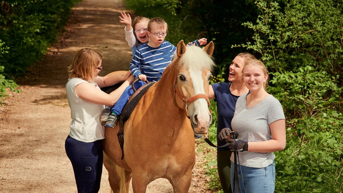 Mehrere Begleiter führen ein Pferd mit darauf zwei Kindern
